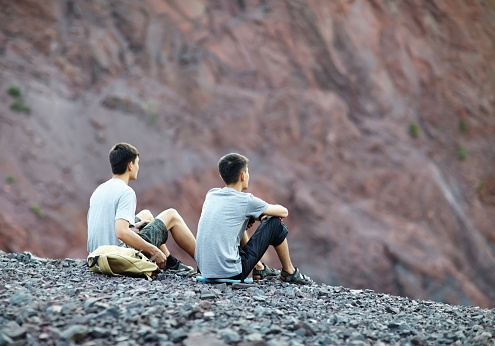 Two tourist young men sitting on rocky cliff and enjoying view