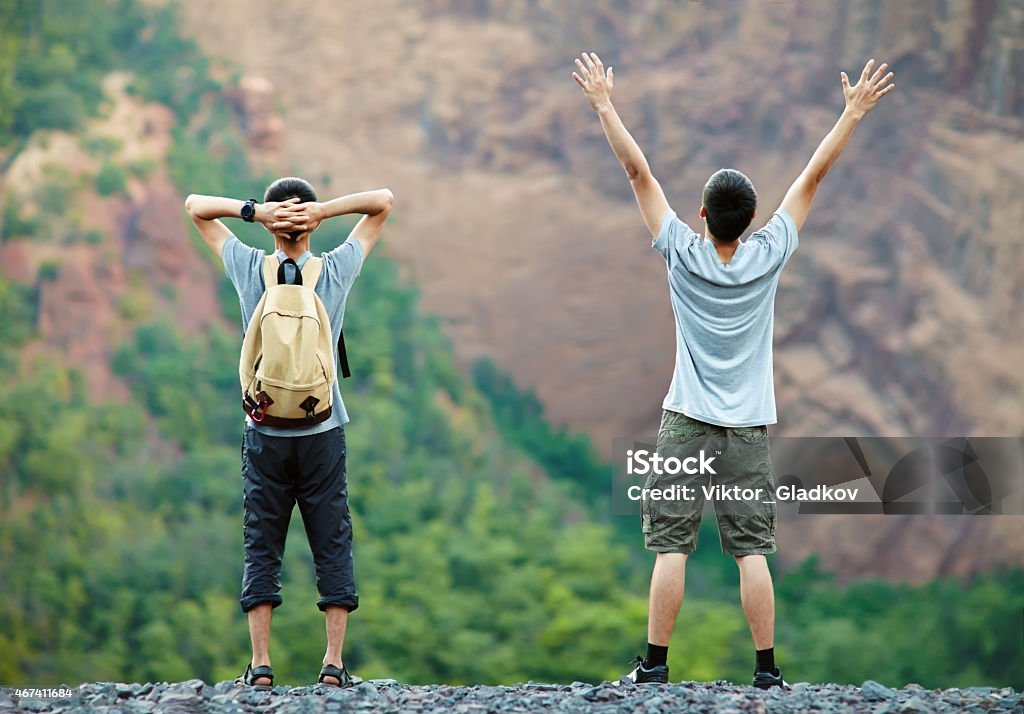 Two happy men enjoying nature Two happy young tourist men standing on rocky cliff and enjoying nature Hand Raised Stock Photo