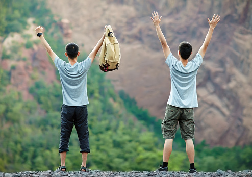 Two young tourist men standing with raised hands on rocky cliff