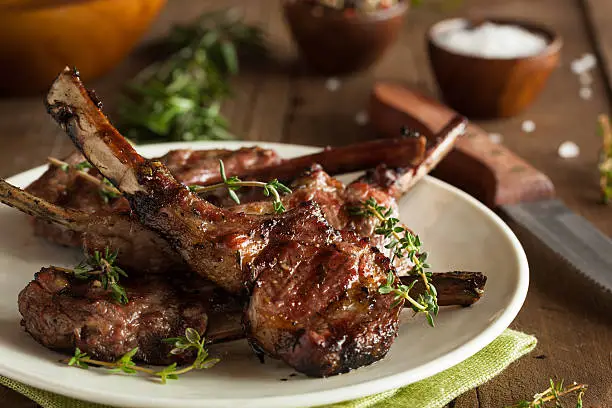 Photo of Grilled lamb chops organized on a white plate on wood