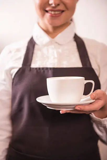 Pretty young barista is offering cup of coffee in a cafe.