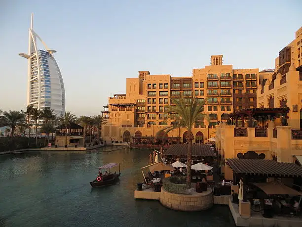 One of the many amazing views in Dubai (UAE), the waterways of Souq Madinat Jumeirah in the shadow of the famous 7 star hotel known as the Burj Al Arab. This photo was taken from a bar in a hotel located right on the coast of Dubai. A perfect place to watch the sun go down while admiring the mixture of older Arabian architecture and modern designs which makes Dubai so unique. An Arbra on the water takes tourists from one end of the complex to the other.