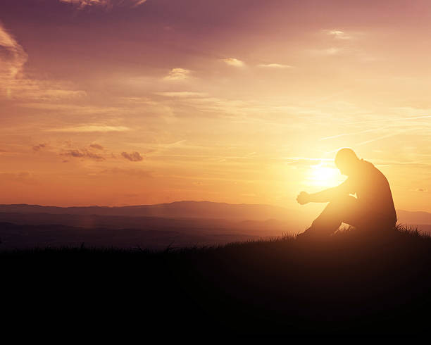 Praying at sunrise Man praying as the sun rises in the mountains. kneeling stock pictures, royalty-free photos & images