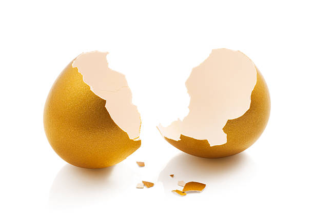 istock Golden egg cracked in half with pieces of shells on white 467440358