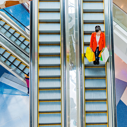 Female shopper standing on escalator with shopping bags in hand.