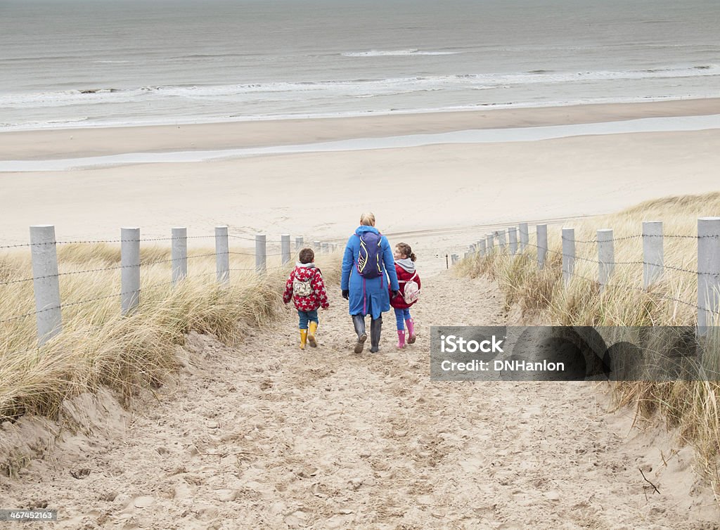 woman and two small children walking down to the beach woman with small boy and girl in winter clothing and rubber boots walking down to a winter beach along a dune path Family Stock Photo