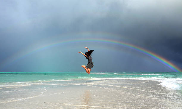 Jumping girl under a rainbow stock photo