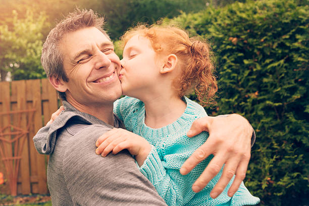 Redhead little girl kissing and hugging father outdoors. Redhead little girl kissing and hugging father outdoors in suburban backyard. leanincollection stock pictures, royalty-free photos & images