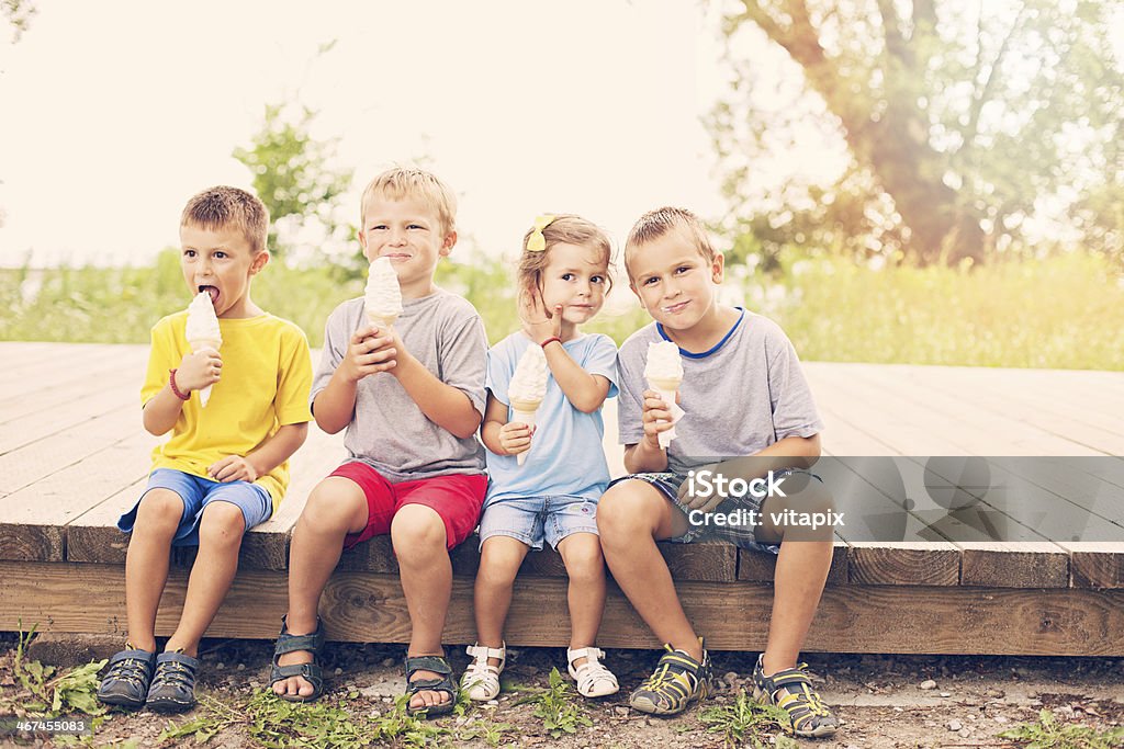 Four happy young children are enjoying icecream cones Four happy young children are enjoying icecream cones, sitting on a wooden boardwalk, with sunlight behind them. 2-3 Years Stock Photo