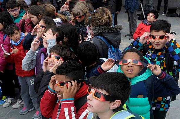 students looking at the solar eclipse Barcelona, Spain - March 20,2015. Children wearing especial protective tinted glasses watching the solar eclipse next to the Barceloneta beach. eclipse stock pictures, royalty-free photos & images