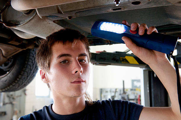 ritratto di un giovane meccanico auto controllo in negozio di riparazione auto - maintenance engineer car lamp protective workwear foto e immagini stock