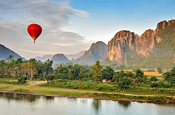 A hot air balloon flying at dawn over the river Nam Song at Vang Vieng, Laos with the scenic backdrop of the karst hill landscape surrounding the town