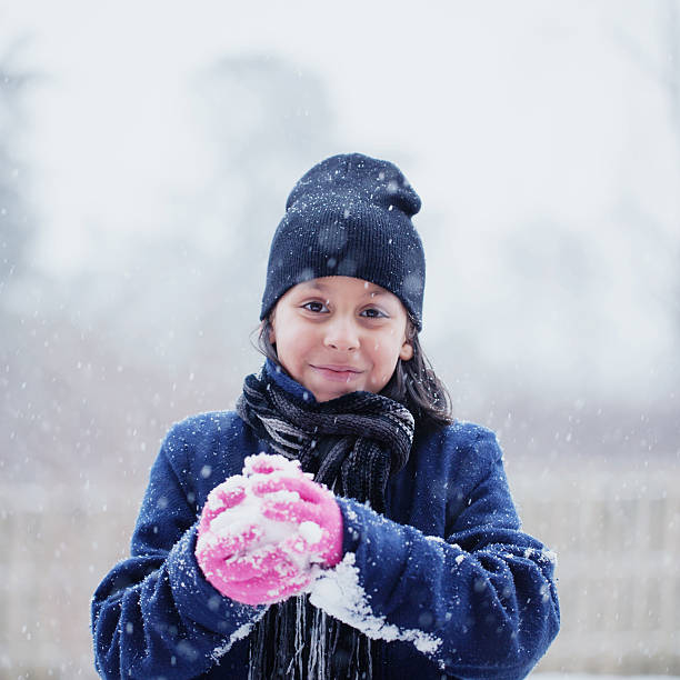 making a snowball Happy little girl playfully in the falling snow. kids winter coat stock pictures, royalty-free photos & images