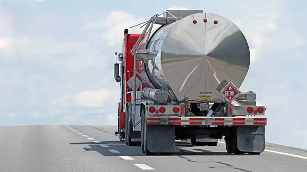 Rear quarter view of a semi tanker truck on a highway hauling a flammable/combustable liquid. Some motion blur with focus on cab. Note reflection of highway on rear of tank. 16:9 aspect ratio.