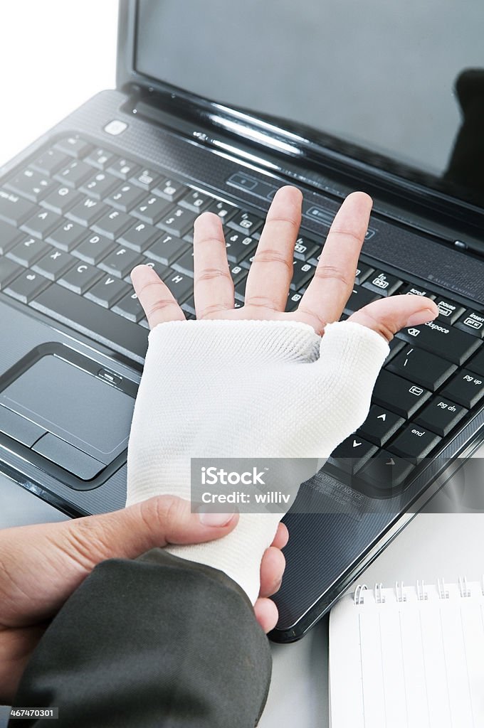 Wrist Pain Woman holds bandaged wrist with laptop keyboard in the background. Adult Stock Photo