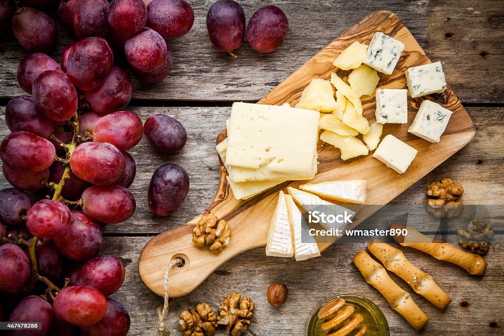 Emmental, Camembert cheese, blue cheese, bread sticks, nuts, honey, grapes Cheese plate: Emmental, Camembert cheese, blue cheese, bread sticks, walnuts, hazelnuts, honey, grapes on wooden table 2015 Stock Photo