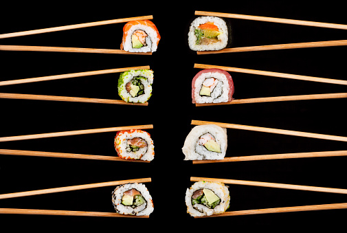Set of sushi pieces in chopsticks, isolated on black background