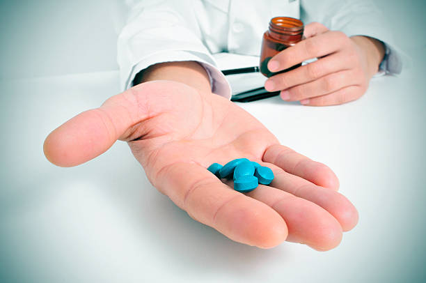 at the doctors office a doctor in a consulting room with a pile of blue pills in his hand medicate stock pictures, royalty-free photos & images