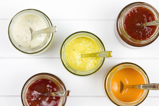 five jars filled with all kind of sauces top-view of five jars filled with curry sauce, tomato sauce, garlic sauce, salsa sauce and whiskey sauce with spoons in it on a wooden surface 1814 stock pictures, royalty-free photos & images