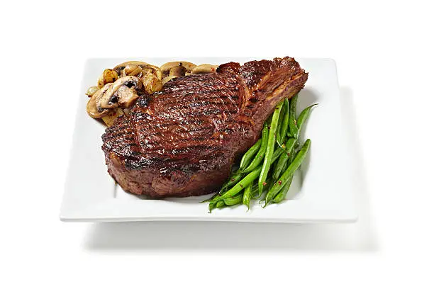 Bone in Rib eye steak with green beans, sauteed mushrooms isolated on a white background.  Professionally shot, silhouetted, color corrected, exported 16 bit and retouched for maximum image quality.