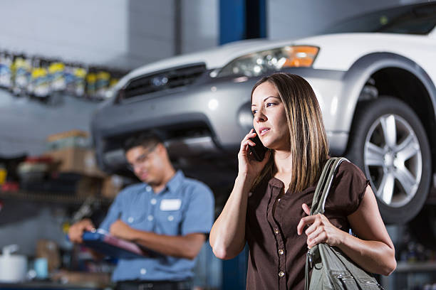 Customer at auto repair shop Hispanic woman (30s) at auto repair shop, with mechanic in background. Focus on woman. car mechanic top view stock pictures, royalty-free photos & images
