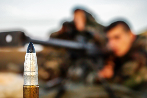 Close-up of a ammunition 12,7 × 99 mm caliber, in the background we can see two sniper fuzzy ready to shot.