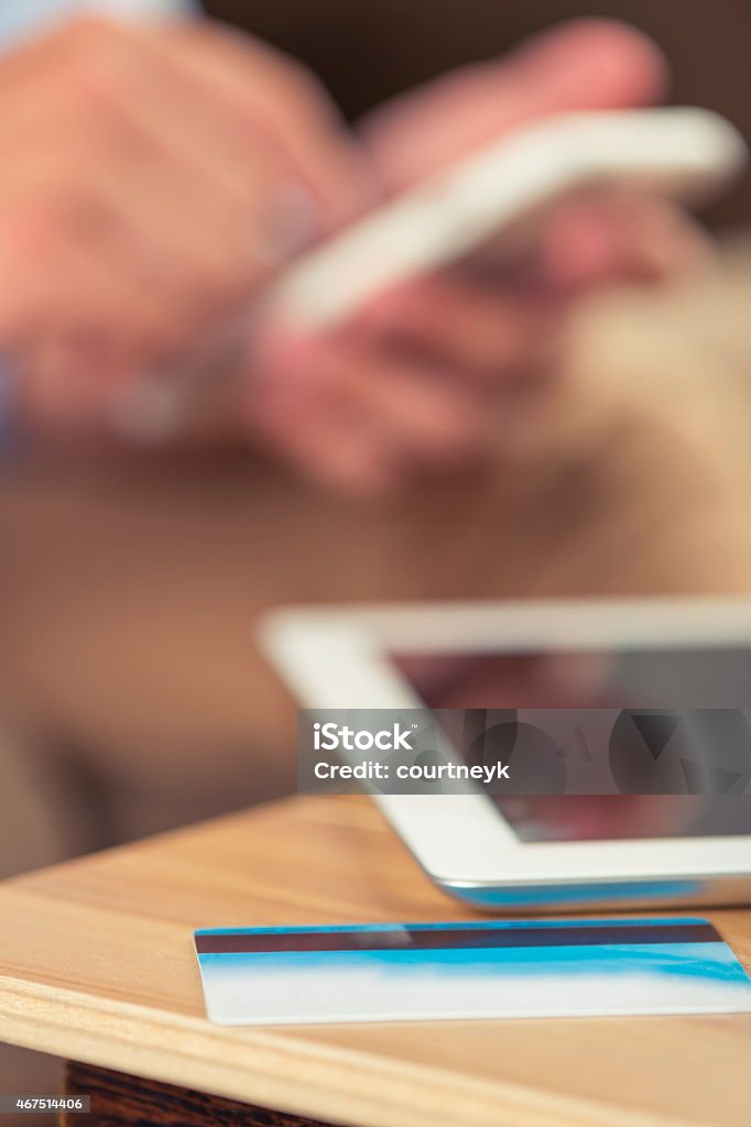 Man with mobile phone, digital tablet and credit card. Man with mobile phone, digital tablet and credit card. Close up of a mans hands. He is holding a smart phone and text messaging or surfing the internet. He is sitting on a sofa wearing a casual clothes and There is a digital tablet and credit card on the table suggesting he is shopping online. 20-29 Years Stock Photo