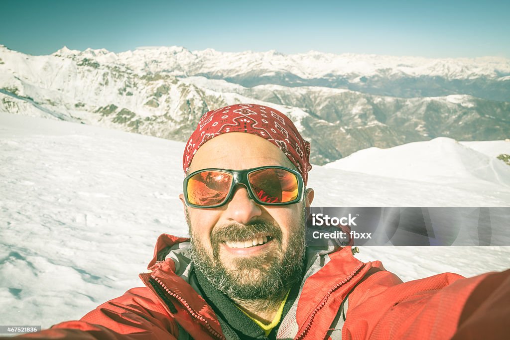 Alpin skier taking selfie Adult european man taking selfie on snowy slope with the beautiful snowcapped italian Alps in the background. Toned image, old retro touch, desaturated. Skiing Stock Photo