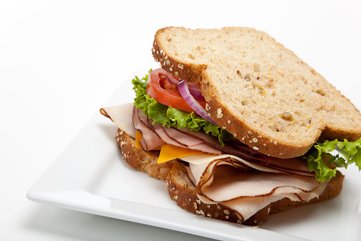 A turkey sandwich on multigrain bread with lettuce, tomato, Cheese and onions on a white background