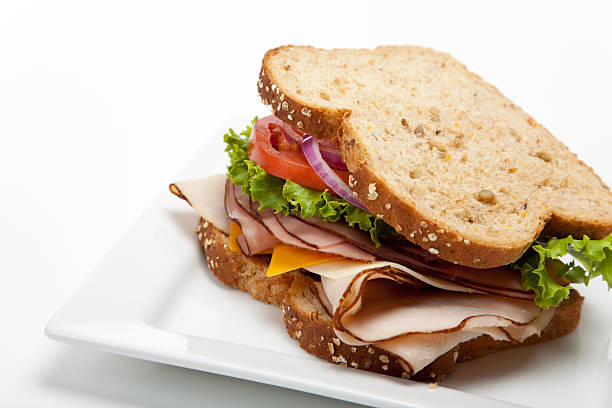 Turkey sandwich on white background A turkey sandwich on multigrain bread with lettuce, tomato, Cheese and onions on a white background delicatessen stock pictures, royalty-free photos & images