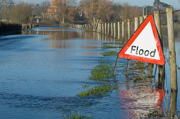 Flooded road and fields A flood warning sign, on a closed country road next to water logged fields in the Avon Valley, Hampshire, England. Flooded after an extreme amount of rainfall at the start of 2014 flood stock pictures, royalty-free photos & images
