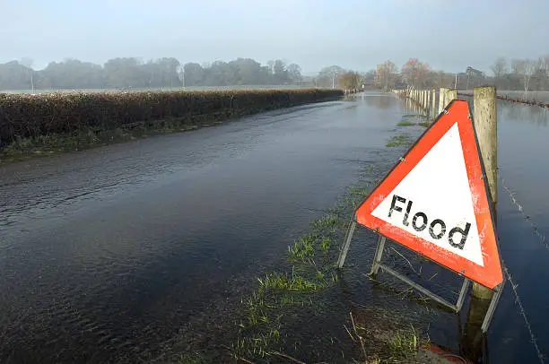 A flood warning sign, on a closed country road next to water logged fields in the Avon Valley, Hampshire, England. Flooded after an extreme amount of rainfall at the start of 2014