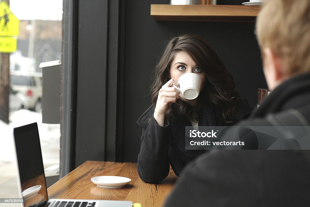 sipping and talking pretty brunette sipping coffee and talking to a friend in a coffee shop Adult Stock Photo