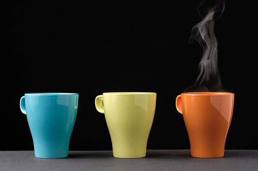 Three colorful mug in a row. One with steam.