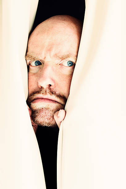 istock Suspicious man frowns through curtains at something unseen 467545501