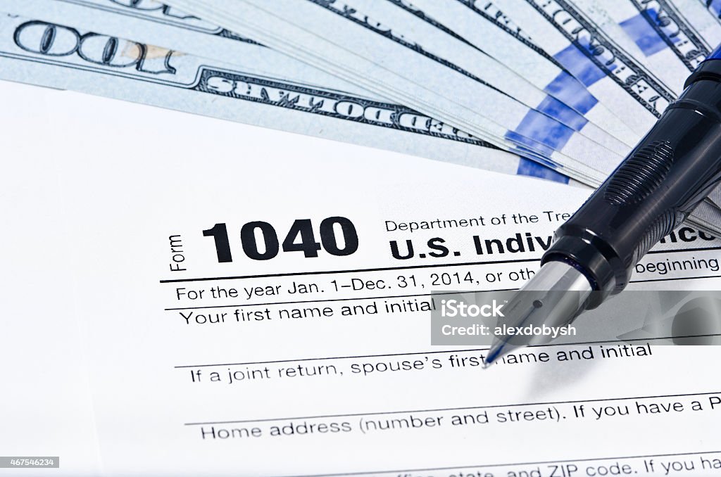 Income Tax Form Tax form 1040 on a gray background, blue pen, and 100 dollar bills out of focus 1040 Tax Form Stock Photo