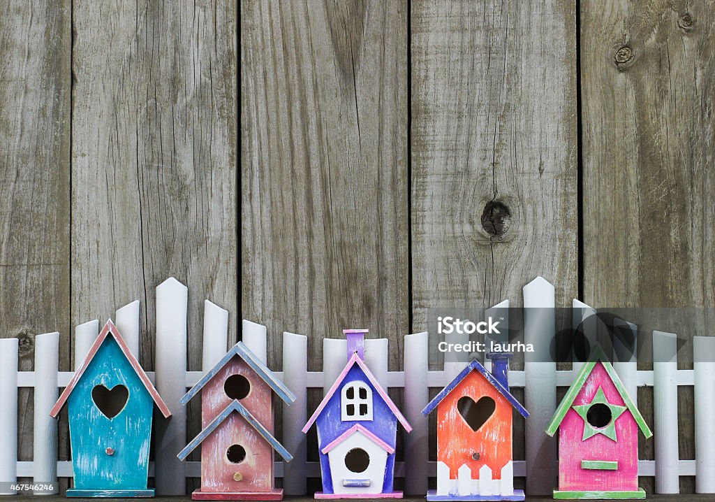 Row of colorful birdhouses by white picket fence Row of colorful spring birdhouses by white picket fence and rustic wooden background In A Row Stock Photo