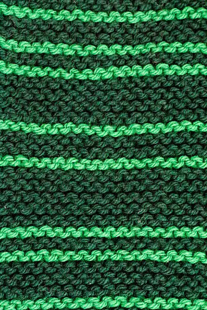 Close up of homemade green knit scarf with light green lines against dark green.