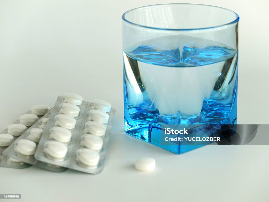 Blisters and a white colored pill with a glass of water. There are some blisters and a white colored pill with a glass of water on white background.The water glass is colored blue. the image was taken as a close up-macro shot in studio on white background.can be use as a health backgrounds on projects.it's called as slogan Take Your Medicine. 2015 Stock Photo