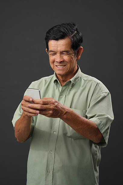 Senior man texting Portrait of smiling senior Vietnamese man texting vietnamese old man portrait stock pictures, royalty-free photos & images