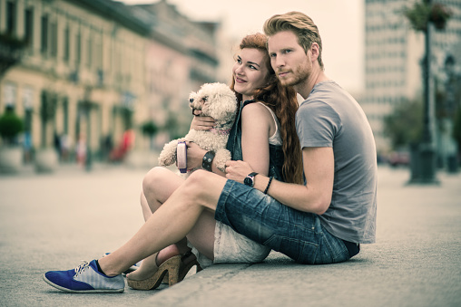 Ginger couple sitting on the sidewalk together with their dog and enjoying the day.