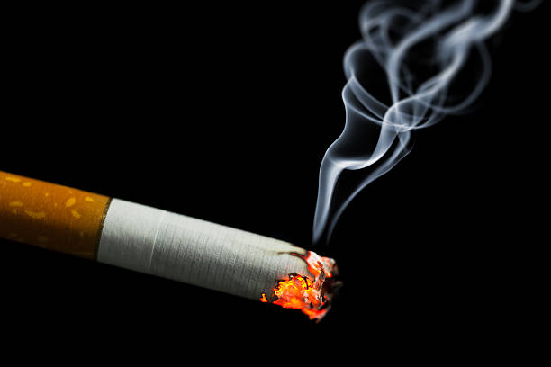 burning cigarette with smoke burning cigarette with smoke on black background cigarette fire stock pictures, royalty-free photos & images
