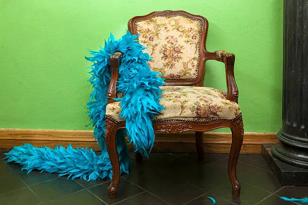 Blue feather boa in the rococo chair on a green background