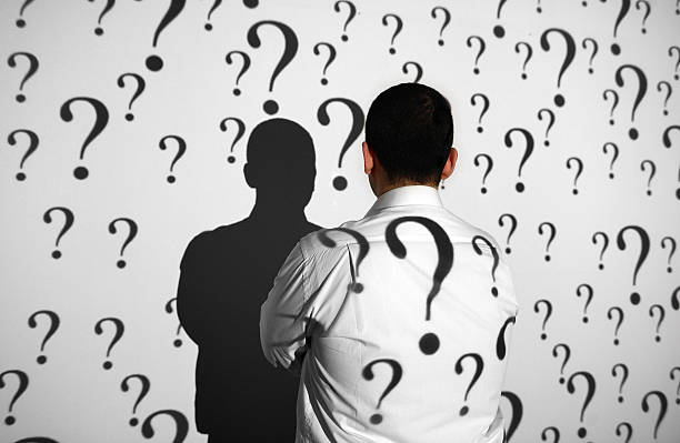 Businessman standing in front of question marks Businessman standing in front of projection screen. Projector reflects questions marks to screen and businessman's back. question mark people one person silhouette stock pictures, royalty-free photos & images