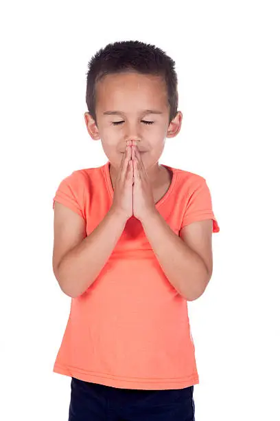little boy with orange shirt and short brown hair with hands in prayer and eyes closed in studio on a white background