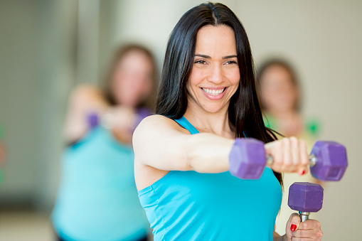A group of female friends exercising with free weights in a health club, following an instructor.