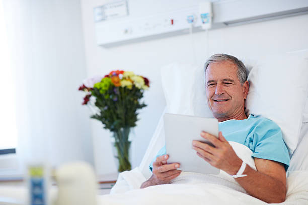 Checking his emails while in hospital Senior patient lying in a hospital bed and using a digital tablet invalid person stock pictures, royalty-free photos & images