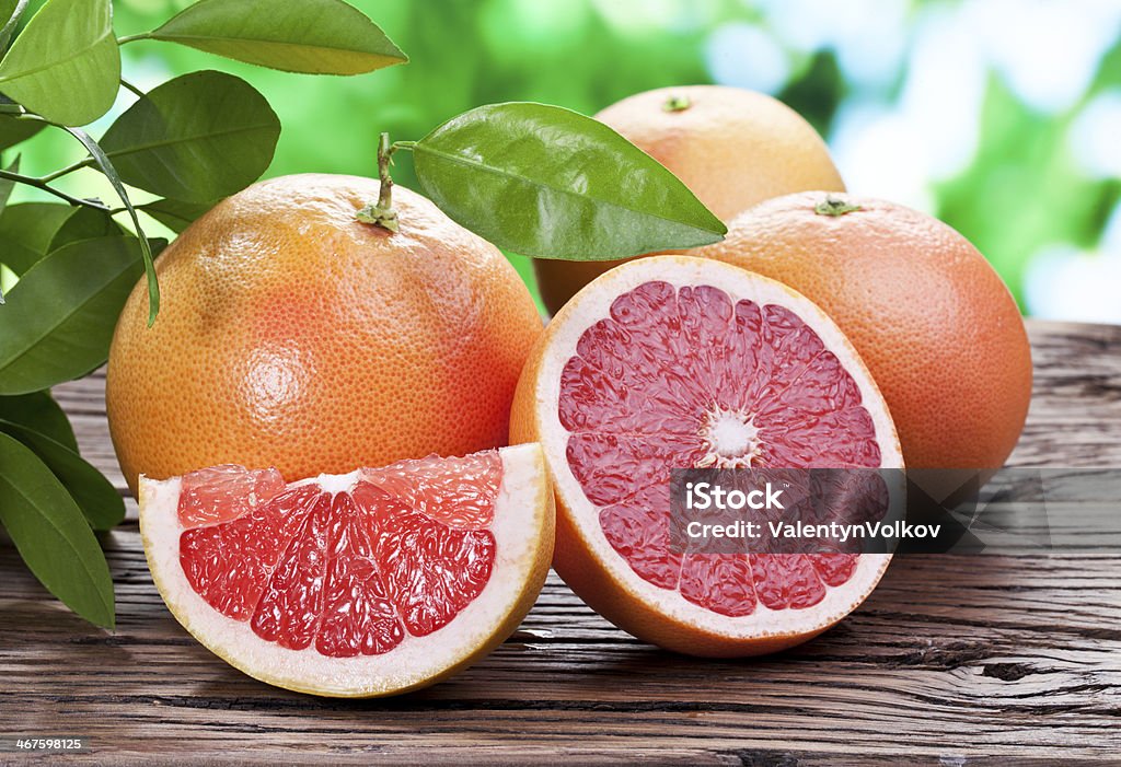 Grapefruits on a wooden table. Grapefruits on a wooden table with green foliage on the background. Grapefruit Stock Photo