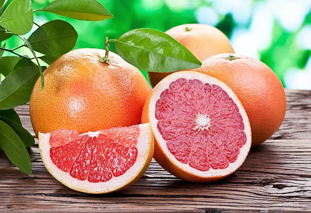 Grapefruits on a wooden table with green foliage on the background.