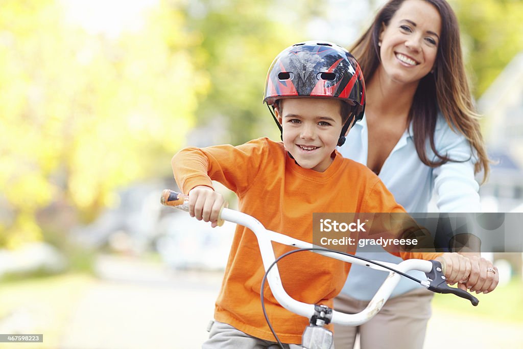 Mom won't let him fall A young mother teaching her son how to ride a bicycle Mother Stock Photo